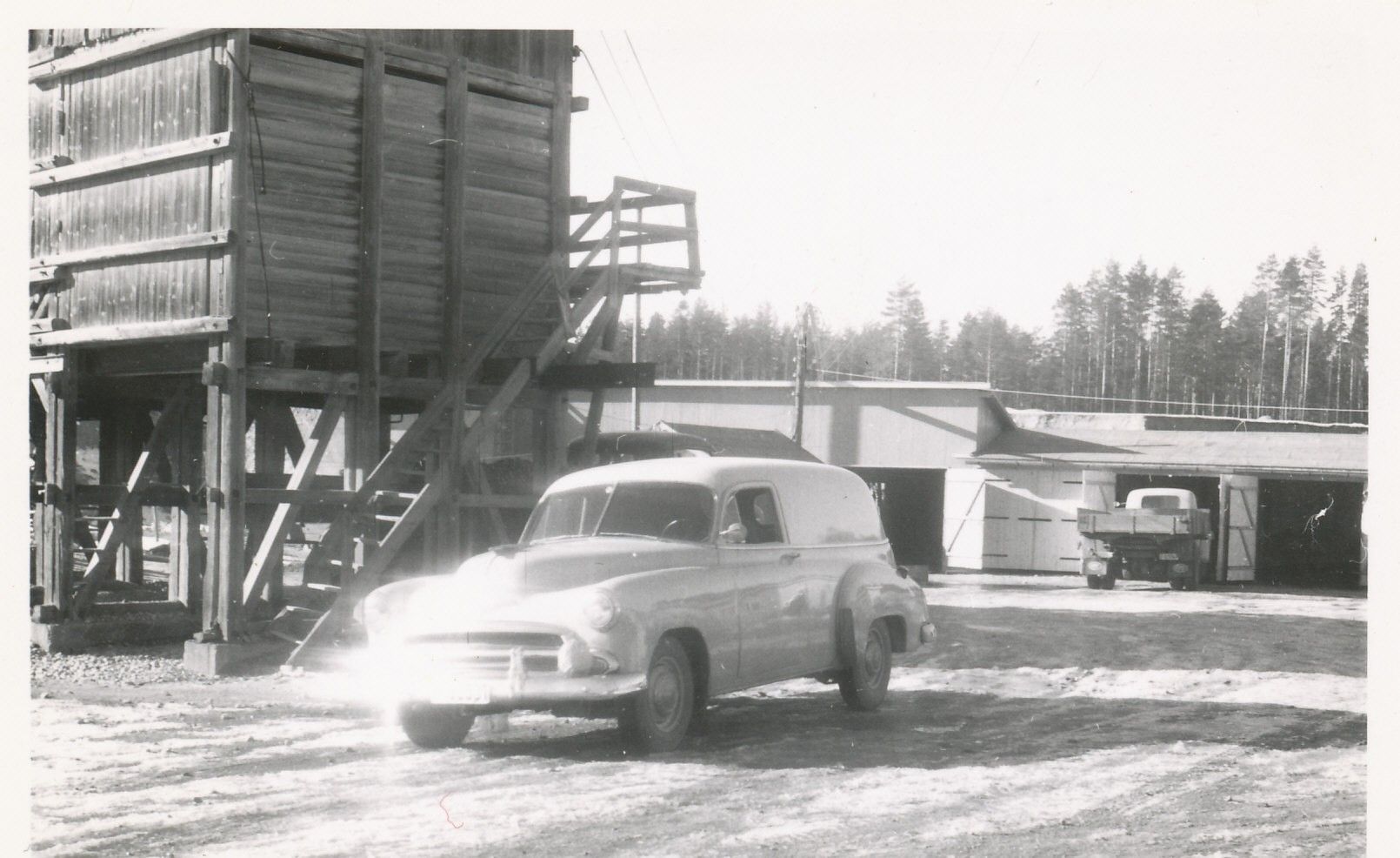 Sort-hvitt bilde av gammel bil ved bygg
